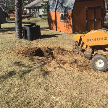 A stump grinder machine removing a tree stump in a yard with a shed in the background.