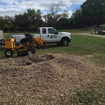 Yard work with a stump grinder and truck in a grassy area.