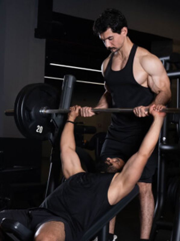 A man bench pressing with a spotter assisting him in a gym.