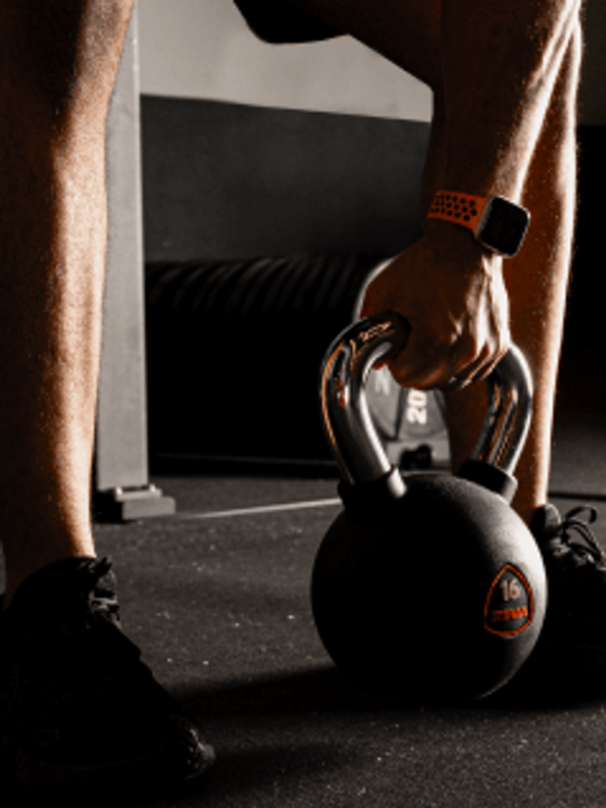 Person lifting a 16 kg kettlebell in a gym with focused lighting.
