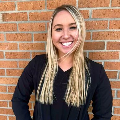 Smiling woman in black top standing against a brick wall.