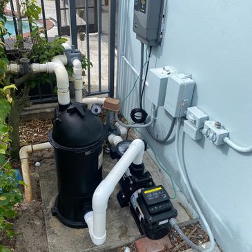 Outdoor pool filtration system with pipes and pump setup against a light blue wall.