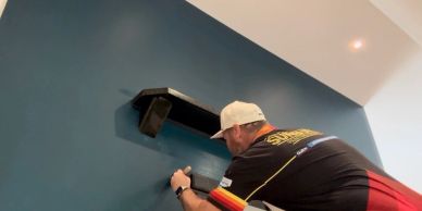 A man installing a black wall shelf on a blue wall.