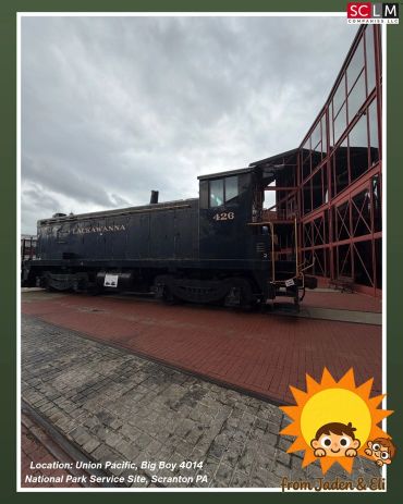 Historic black train engine displayed outdoors on a cloudy day.