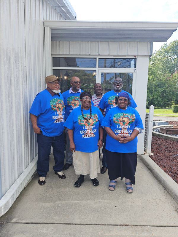 Group of smiling people wearing matching blue "I am my brother's keeper" shirts.