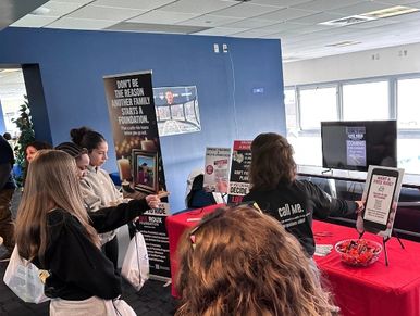 People gather around a booth with informative displays and red tablecloth.