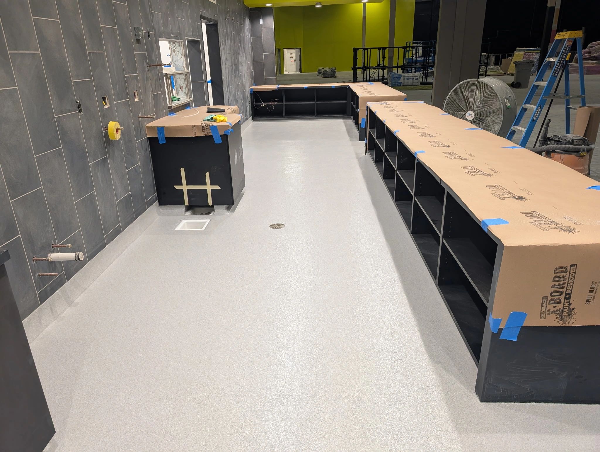 Under-construction room with covered counters, grey tiled walls, and a ladder.