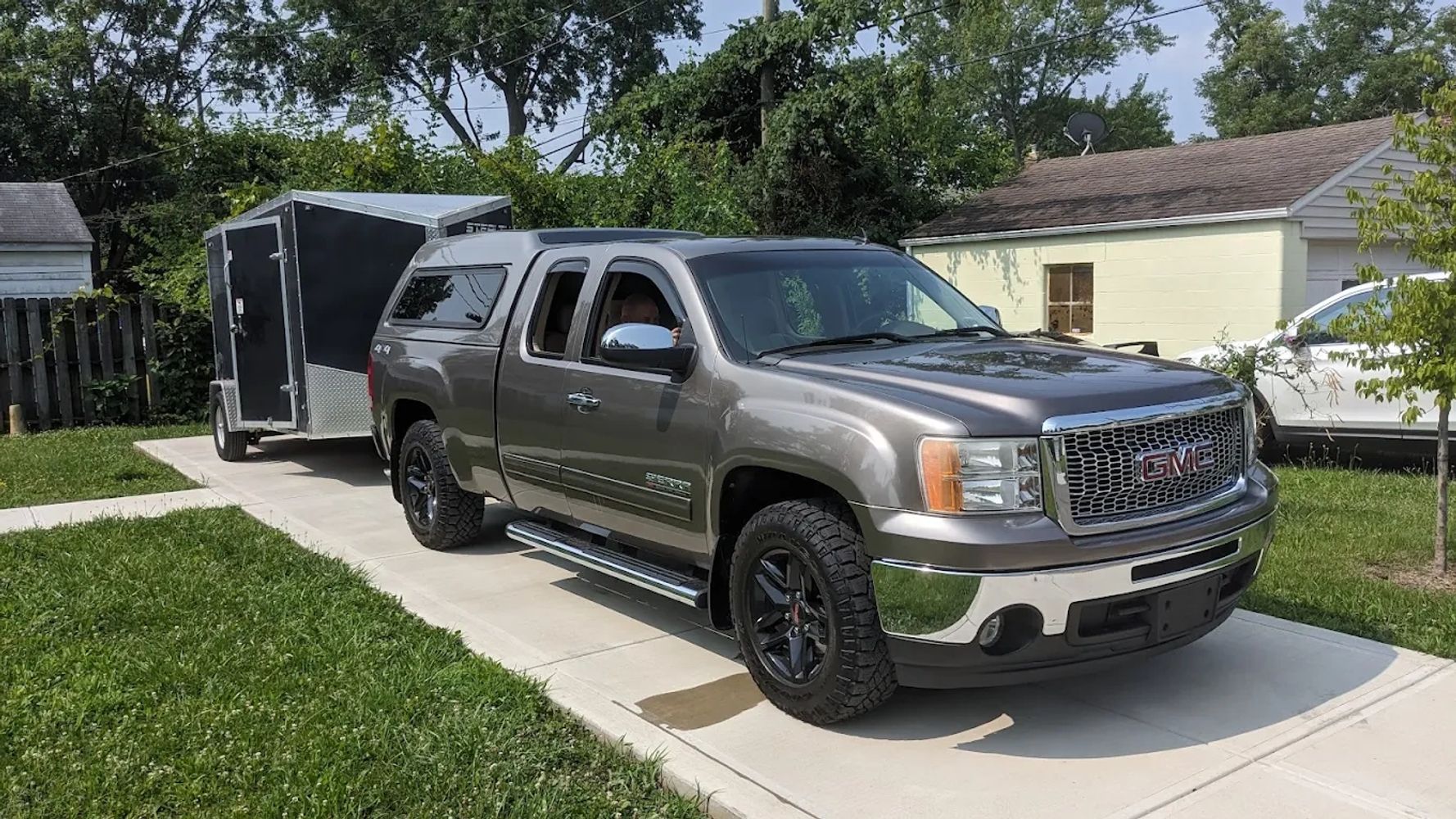 GMC pickup truck towing a black enclosed trailer on a driveway.