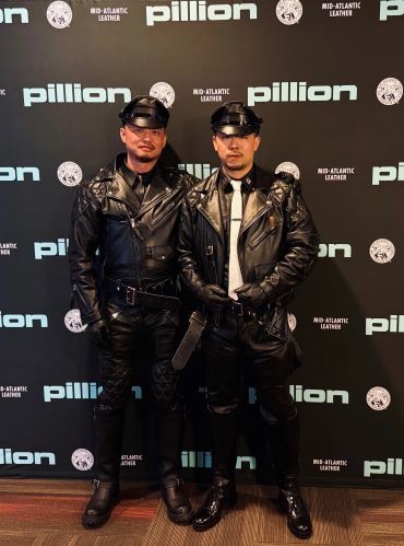 Two men dressed in black leather outfits at a promotional event.