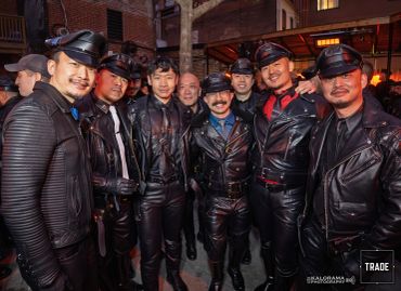 Group of men in leather attire posing outdoors at night.