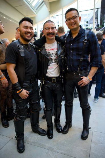 Three men dressed in black leather outfits smiling indoors.