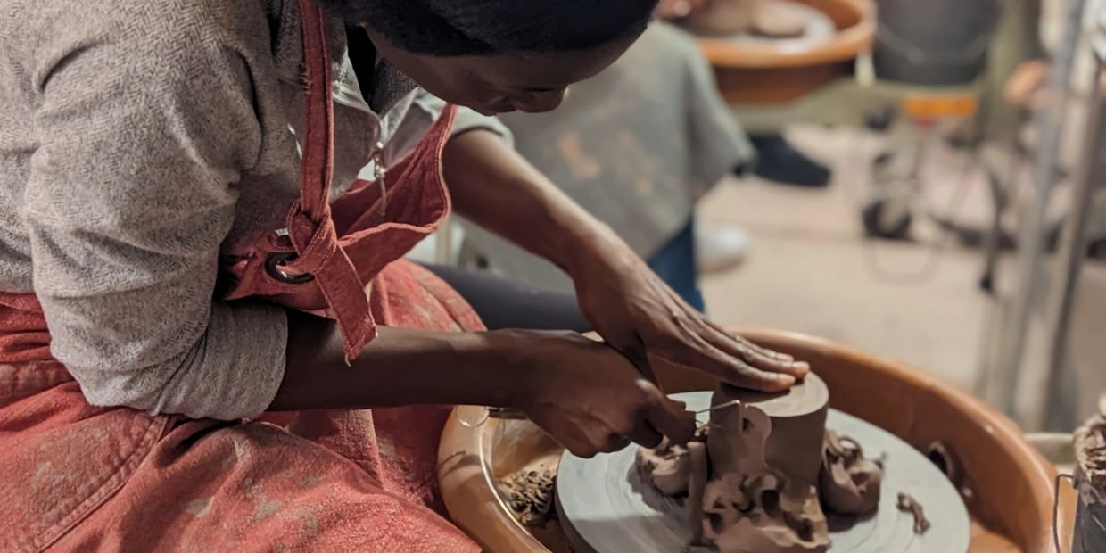 Person shaping clay on a pottery wheel with focused hands.