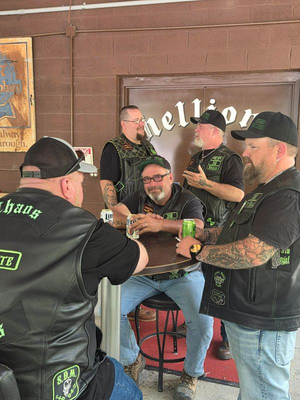 Bikers with tattoos and leather vests socializing over drinks at a bar.