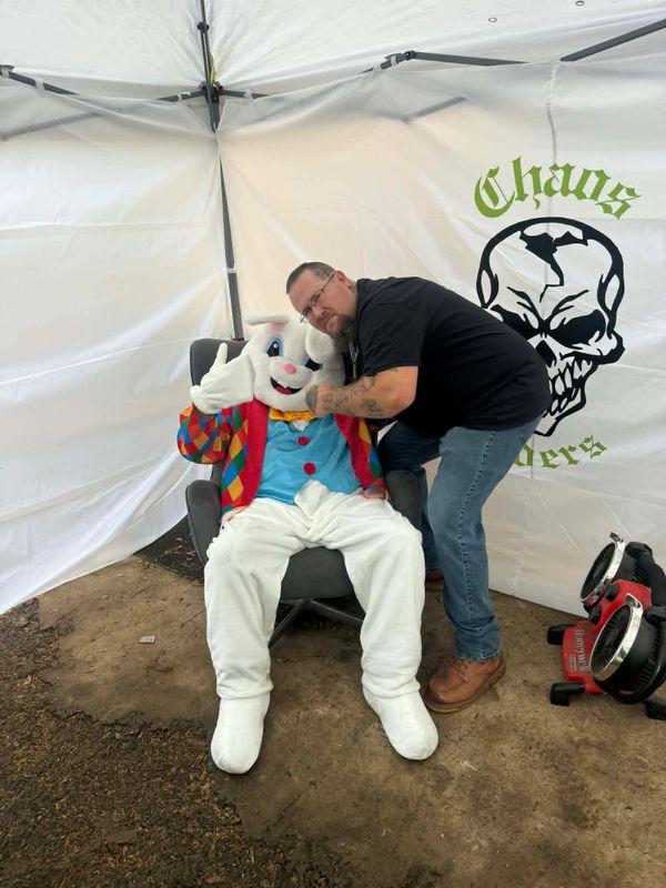 Man posing with a person in a colorful Easter bunny costume inside a tent.