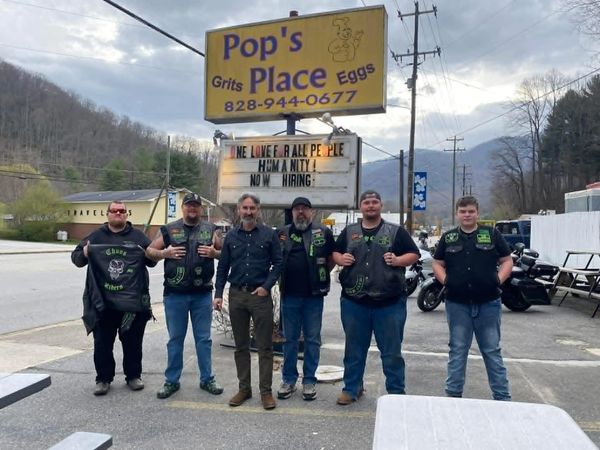 Six men stand outside Pop's Place restaurant under a sign about love and hiring.