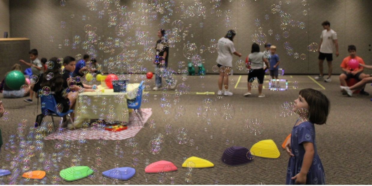Children playing indoors with bubbles and colorful toys scattered around.