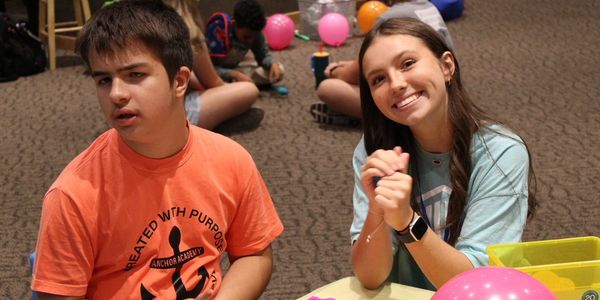 Two teenagers sitting on the floor, one smiling and the other looking away.
