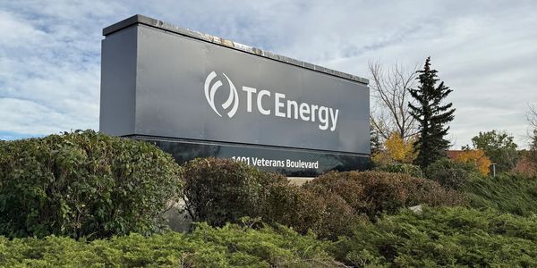 Sign for TC Energy surrounded by bushes under a cloudy sky.