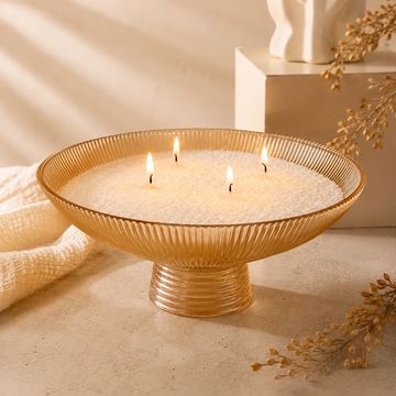 Vela decorativa con cuatro mechas en un recipiente dorado.