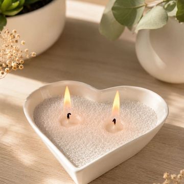 Vela de dos mechas en forma de corazón encendida.