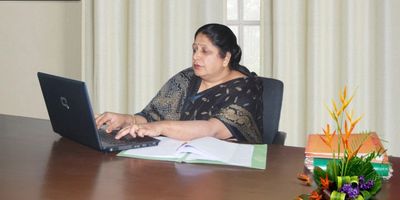 Woman working on a laptop at a desk with documents and flowers.