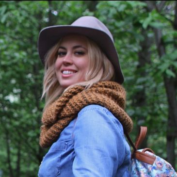 Smiling woman in a hat and scarf outdoors with a backpack.