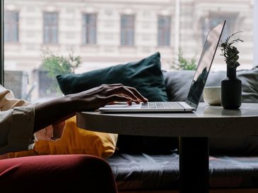 Person typing on a laptop at a cozy table near a window.