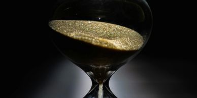 Close-up of a dark hourglass with golden sand flowing through its narrow neck.