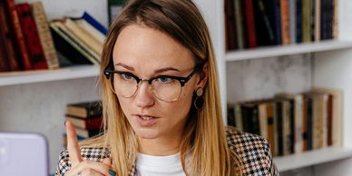 A woman with glasses explaining something with her finger raised.