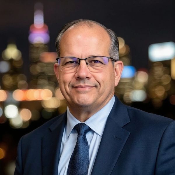 Professional man in glasses and suit with city lights blurred in background.