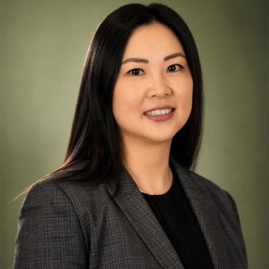Professional woman in a gray blazer with a black shirt against a green background.