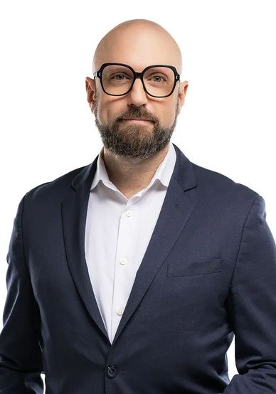 Bald man with beard wearing glasses and a navy blue suit.