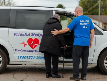 A caregiver assists an elderly person with a cane into a van.