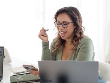 Woman excitedly looking at her phone while working on a laptop.