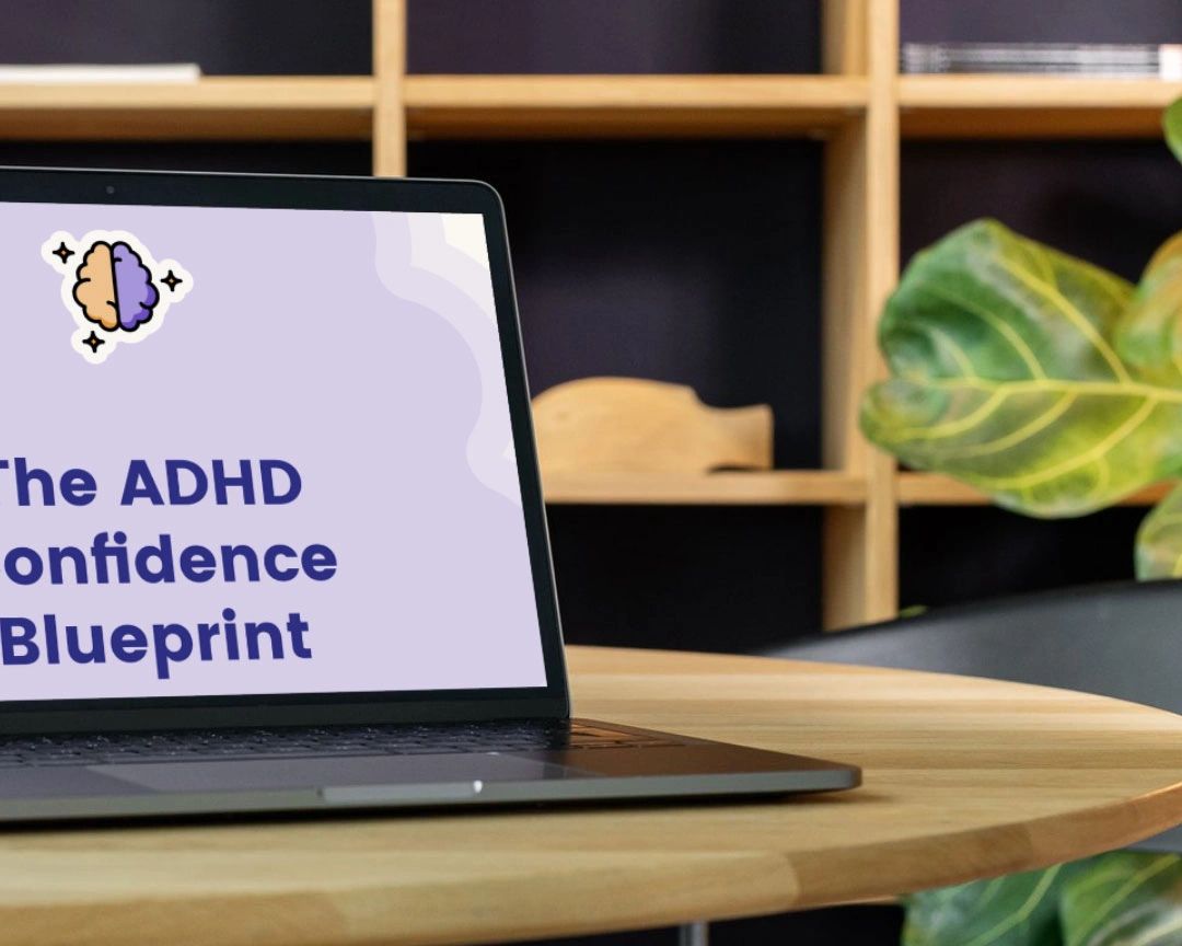 Laptop sitting on wooden desk. Screen shows eBook cover of The ADHD Confidence Blueprint.