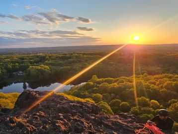 Sunset over a forest with a rocky cliff and a person sitting.