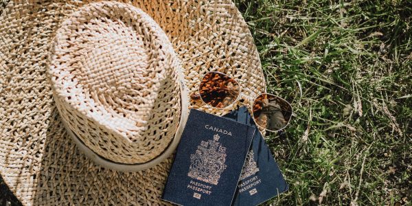 Two Canadian passports, straw hats, and sunglasses on grass.
