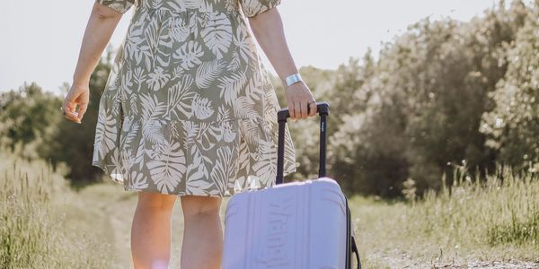 Person walking on a dirt path pulling a suitcase.
