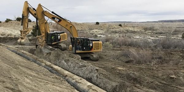 Two pieces of construction equipment moving a large pipeline.