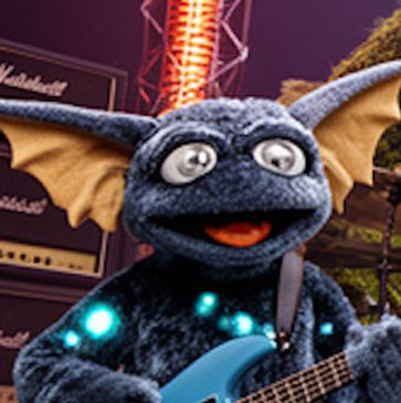 A blue puppet with large ears playing an electric guitar.