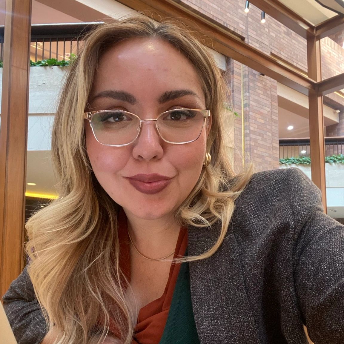 Woman with glasses smiles indoors in a cozy setting.