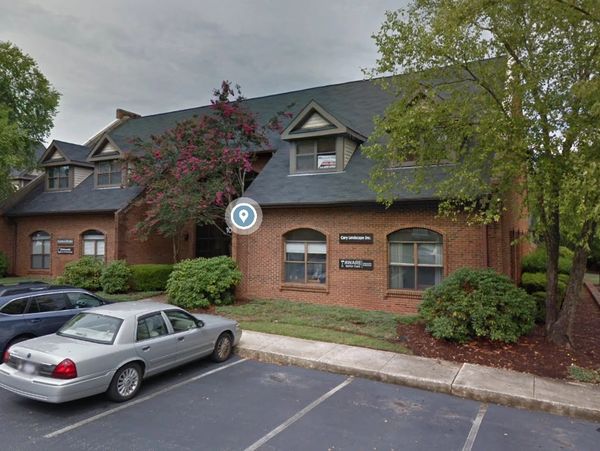 Brick office building with cars parked outside under cloudy sky.