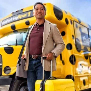 Man with a yellow suitcase standing in front of a yellow bus.