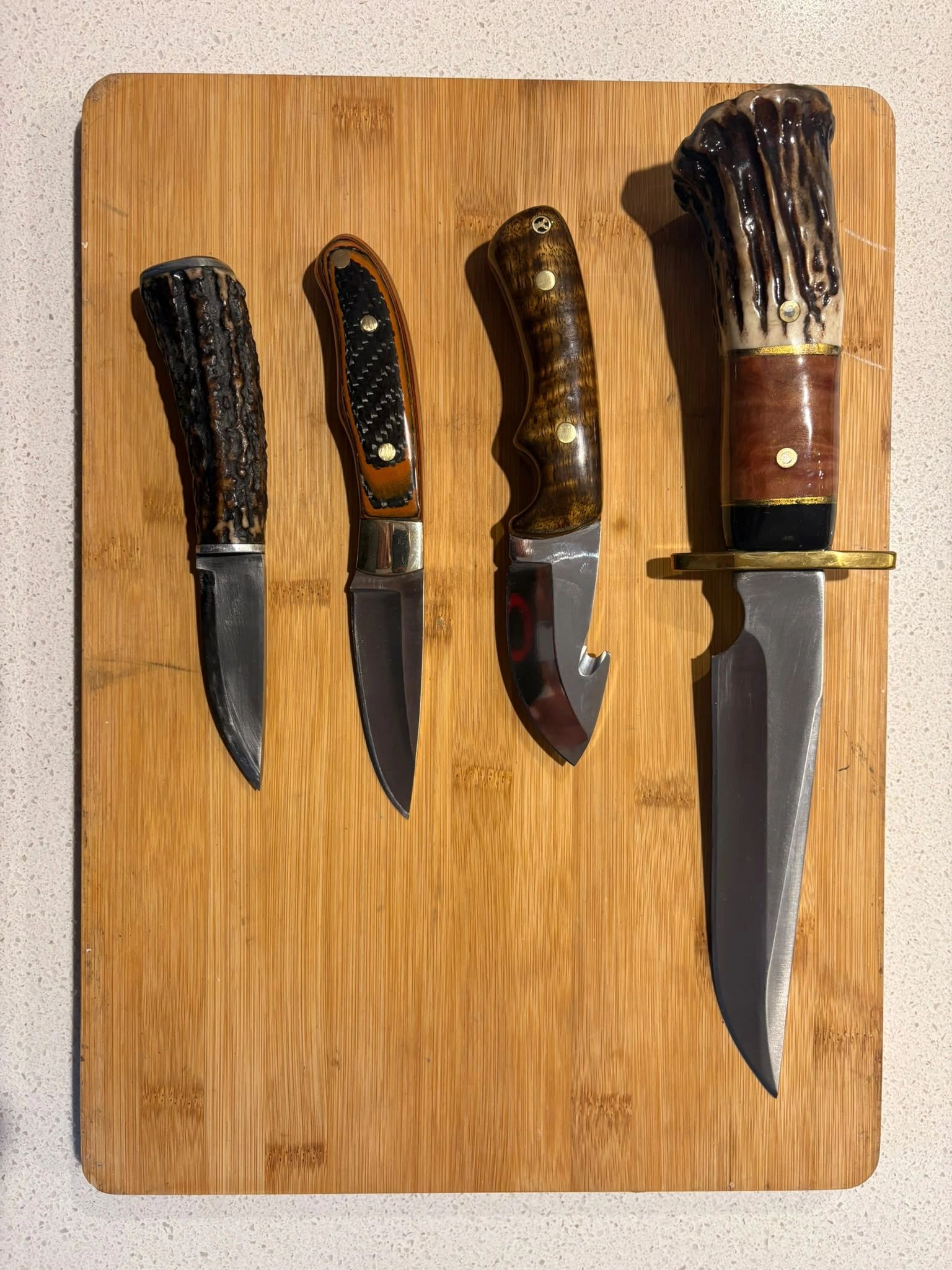Four hunting knives with varied handles on a wooden board.