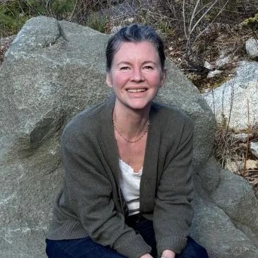 Smiling woman sitting on a rock outdoors.