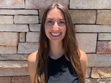 Young woman with long hair smiles brightly against a stone wall background.