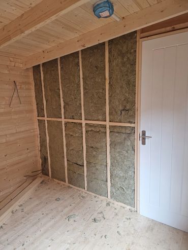 Partially insulated wooden interior wall with a white door.