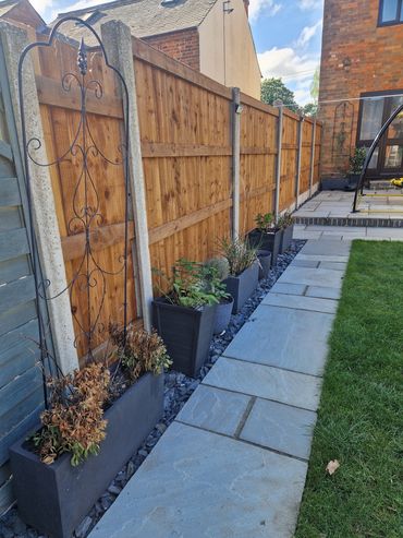 A neat garden pathway with potted plants along a wooden fence.
