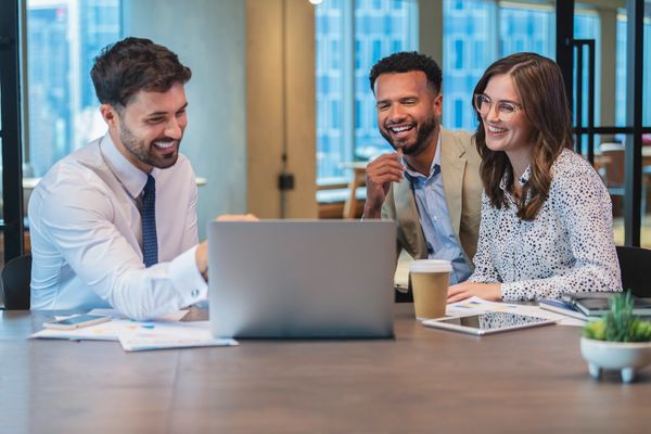 A diverse group of professionals engaged in a discussion around a laptop at a modern office space