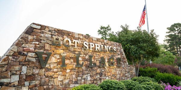 Stone sign reading 'Hot Springs Village' surrounded by greenery and flowers.
